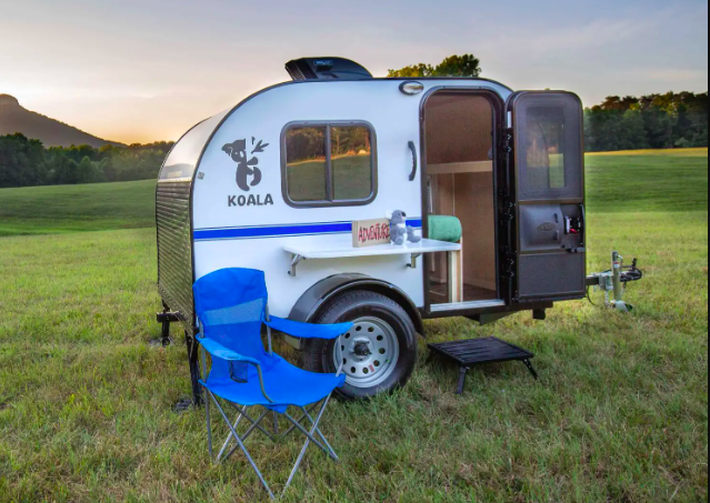 Rustic Trail teardrop camper set up in a green field with a camping chair out the front.