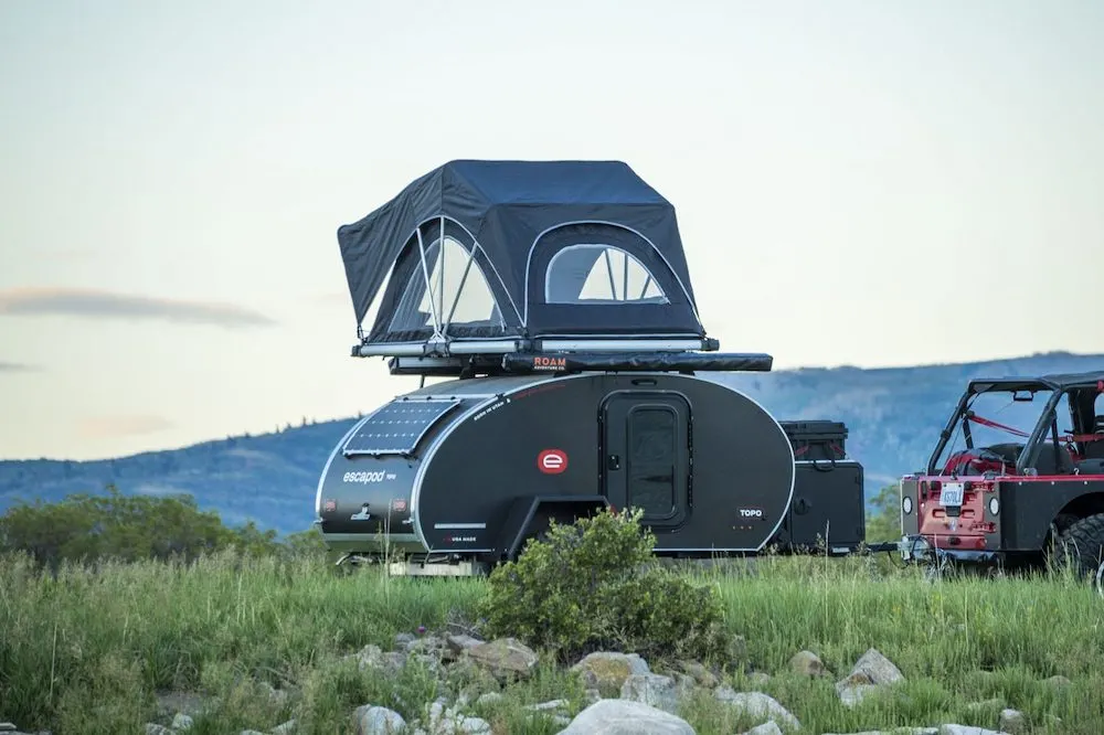 Small teardrop camper with roof top tent set up in a remote area