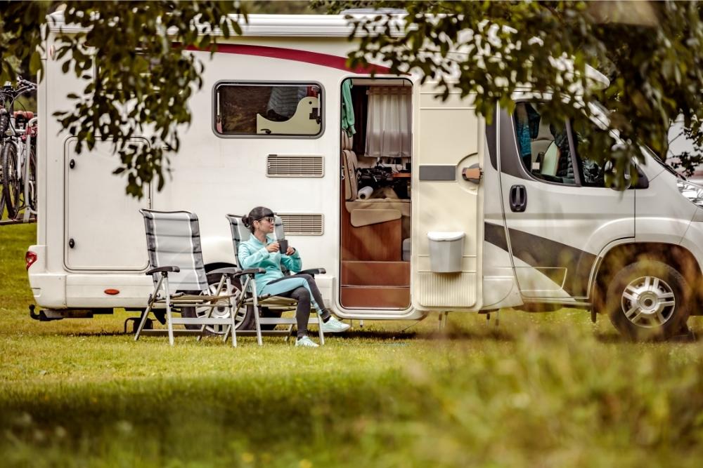 Woman sitting outside an RV in a camp chair with a drink in hand.