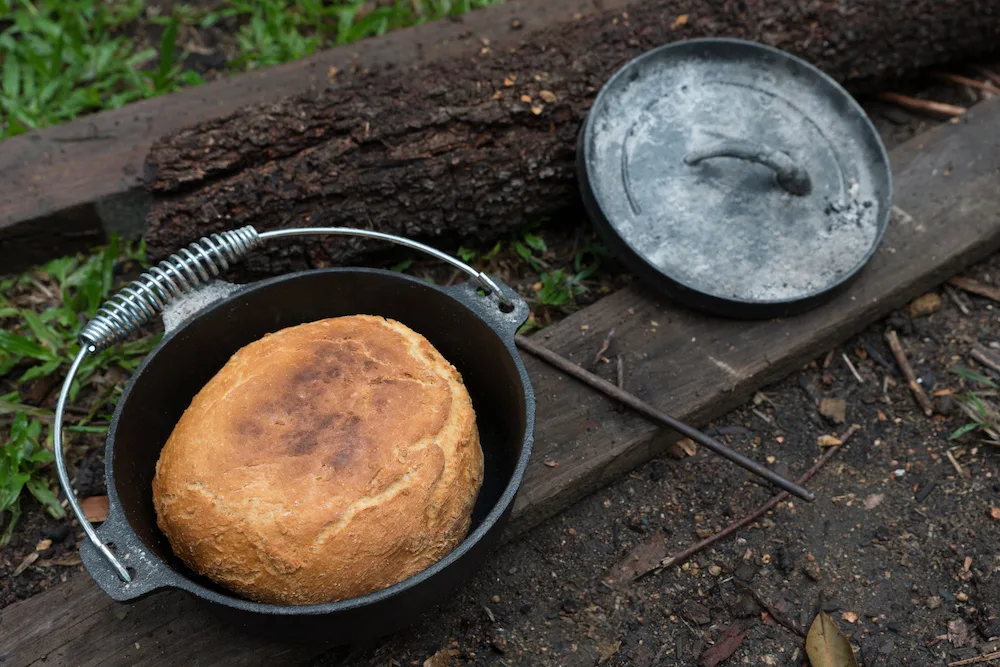 Dutch oven with the lid off showing cooked damper bread inside.