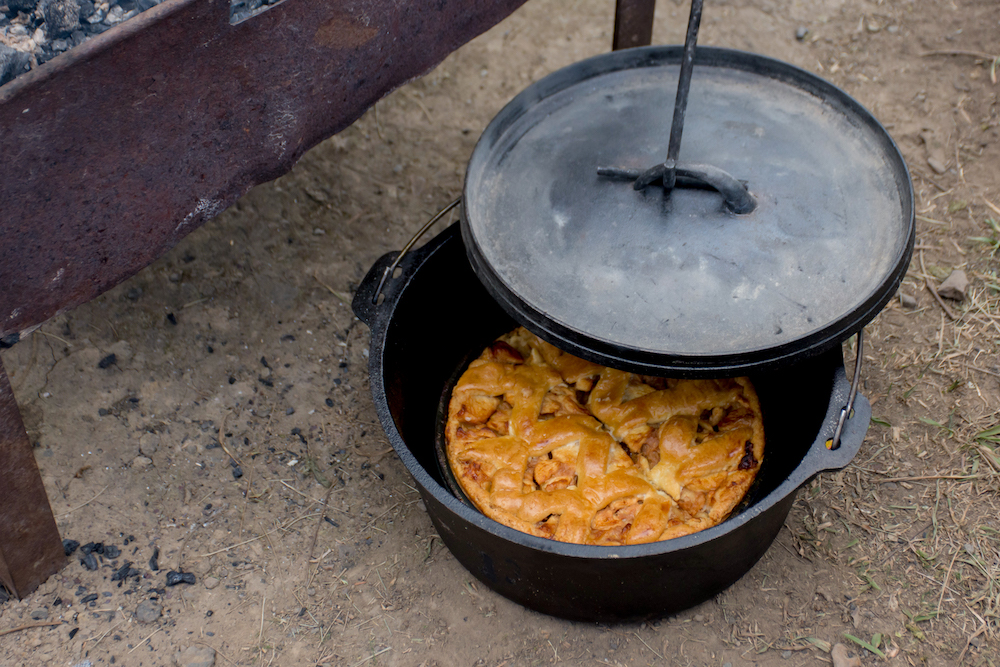 Dutch oven with the lid ajar showing a cooked apple pie inside.