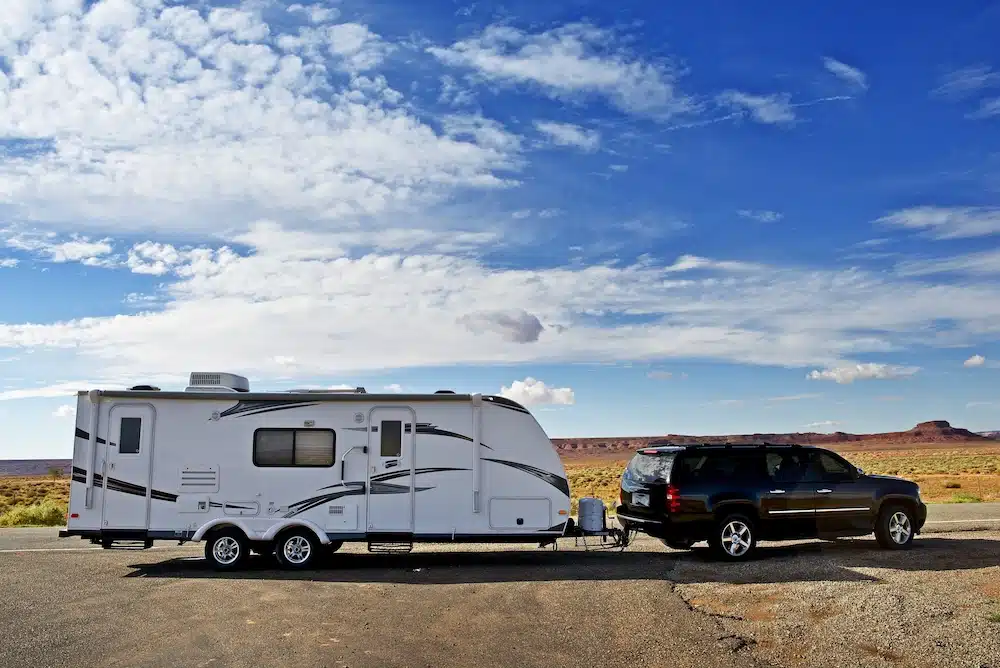 Car towing a travel trailer parked in desert area.