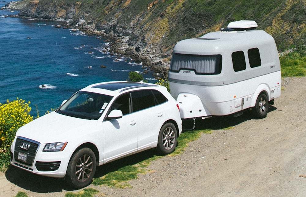 White car and fiberglass caravan parked at a coastal view