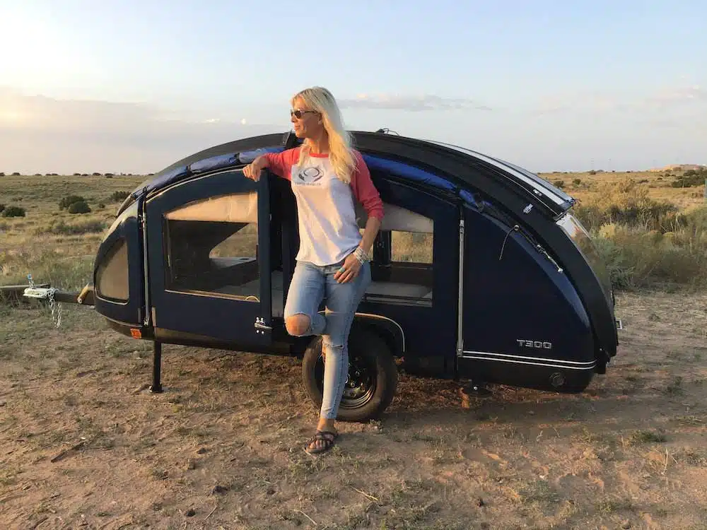 Woman standing beside a small teardrop camper